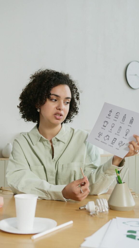 A young woman explains concepts using illustrated educational materials at a table indoors.